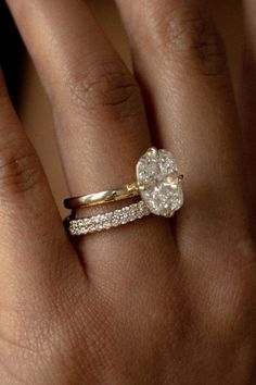 a woman's hand with a diamond ring on top of her finger and the other hand holding an engagement ring