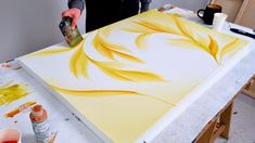 a person is painting on a canvas with yellow and orange colors in an art studio