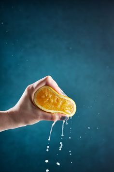 a person holding an orange in their hand with water coming out of it to the side