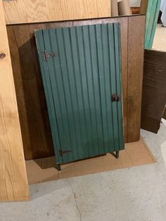 a green metal door sitting inside of a wooden cabinet next to a pile of wood