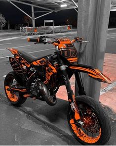 an orange and black dirt bike parked next to a pole