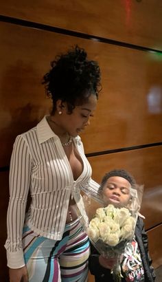 a woman standing next to a little boy holding a bouquet of flowers in his hand