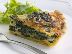 a piece of quiche with spinach and bacon on it next to a salad