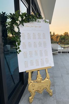 a wedding seating chart on a gold easel in front of a window at sunset