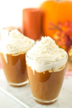 two glasses filled with dessert sitting on top of a white tray next to an orange pumpkin