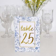 there is a table number with wine glasses and flowers in the vase on the table