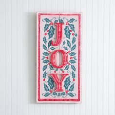 a red and white christmas card with the word joy hanging on it's side