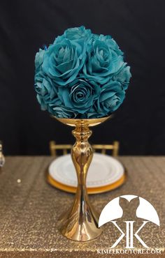 a gold vase filled with blue flowers on top of a table next to a plate