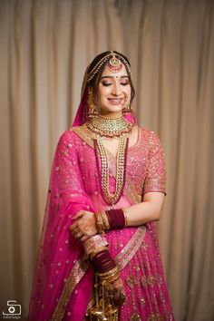 a woman in a pink bridal outfit and gold jewelry is posing for the camera