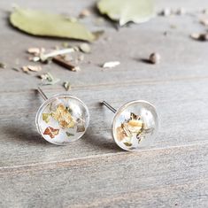 two small glass studs with dried flowers in them sitting on a wooden table next to leaves