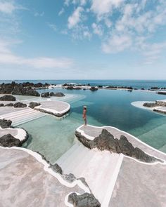 a person standing on the edge of a body of water surrounded by rocks and sand