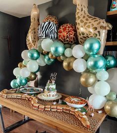 a table topped with lots of balloons and cake next to a giraffe statue