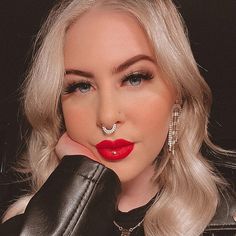 a woman with blonde hair and red lipstick wearing black leather gloves, holding her hand to her face