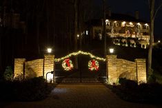 a gate with christmas wreaths and lights on it in front of a large house