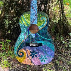 a colorful guitar sitting in the grass next to a tree with leaves and swirls on it