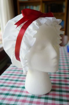 a white mannequin head with a red ribbon on it's head sitting on a checkered table cloth