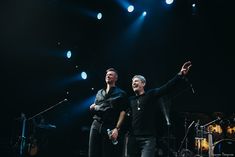 two men standing next to each other in front of microphones and drums on stage