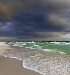 an ocean beach with waves coming in to shore and dark clouds above the water on a cloudy day