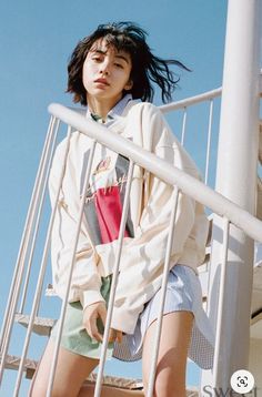 a young woman sitting on top of a metal hand rail next to a white pole