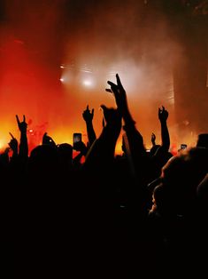 a crowd of people at a concert with their hands up in the air and lights on