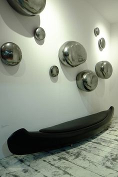 a wall with several metal balls on it and a black bench in front of it