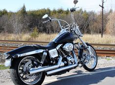 a motorcycle is parked on the side of the road next to train tracks and trees