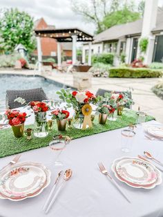 the table is set with flowers and place settings for an outdoor dinner by the pool