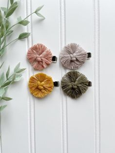 three different colored hair clips on top of a white table next to a plant and some leaves