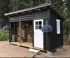 a small black shed with some flowers on the outside and wood stacked up in front