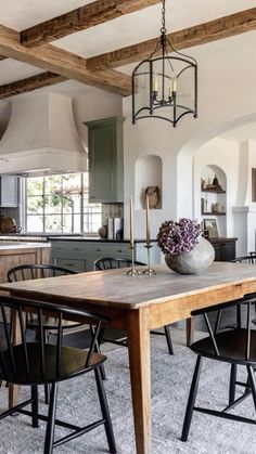 a dining room table and chairs in front of an open kitchen area with exposed beams