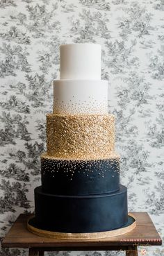 a three tiered cake with black, white and gold frosting on a wooden stand