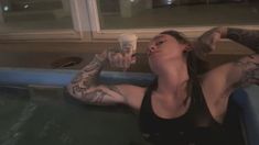 a woman in a bathtub with her arms up and eyes closed, drinking from a cup