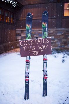 two skis sticking out of the snow next to a sign that says cocktails this way