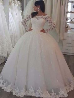 a woman standing in front of a mirror wearing a white wedding dress with long sleeves