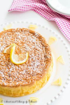 a lemon cake with powdered sugar on top sits on a white plate next to a pink and white checkered table cloth