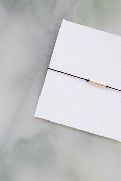 a white card with a black string and a gold beaded bracelet on top of it