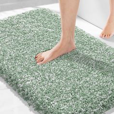 a person standing on top of a green rug next to a bathtub and toilet