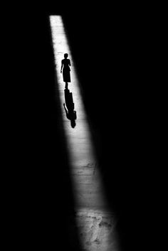 a person with a suitcase is walking in the dark, casting a long shadow on the floor