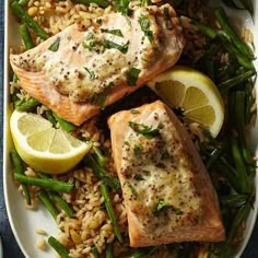 two salmons, rice and asparagus on a plate with lemon wedges