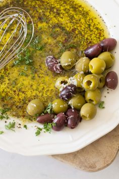 olives and parsley in a white bowl with a whisk on the side