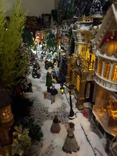 a toy town with lots of buildings and people walking around it in the snow at night