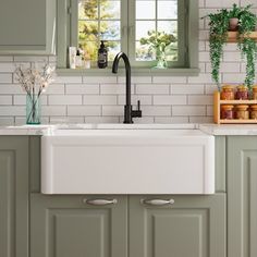 a white kitchen sink sitting under a window next to green cupboards and counter tops