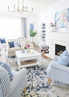 a living room filled with furniture and a fire place under a chandelier in front of a window