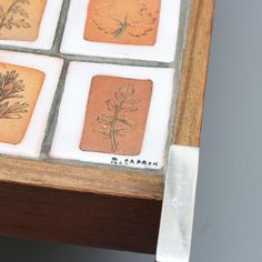 four square tiles with plants on them are sitting on a wooden table next to a knife