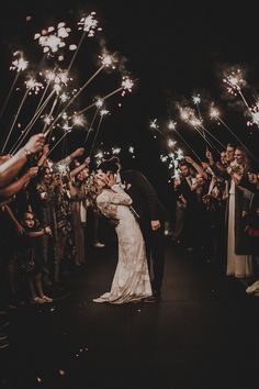 a bride and groom kissing under sparklers at night in front of their wedding guests