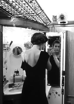 a woman in a black dress looking at herself in the mirror