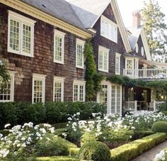 a large brown house with white trimmings and lots of flowers in the front yard