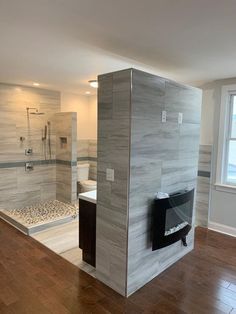 an empty bathroom with wood flooring and white tile on the walls, along with a walk in shower