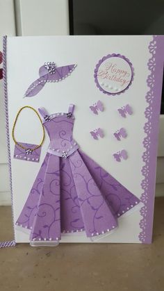 a birthday card with a purple dress and butterfly decorations on the front, sitting on a table