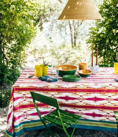 a table with plates and bowls on it in the middle of some bushes, under a hanging light fixture